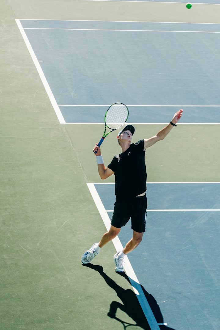 Joueur de tennis en t-shirt noir au lancer de balle de son service, raquette armée derrière la tête